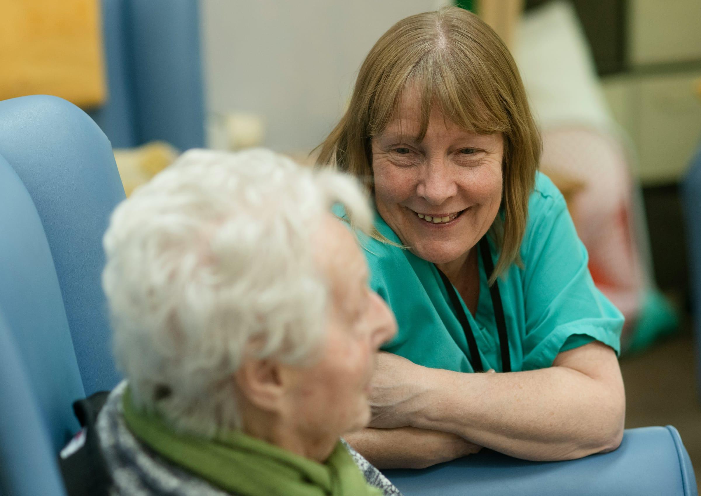A care worker in uniform sitting and talking with an older resident.