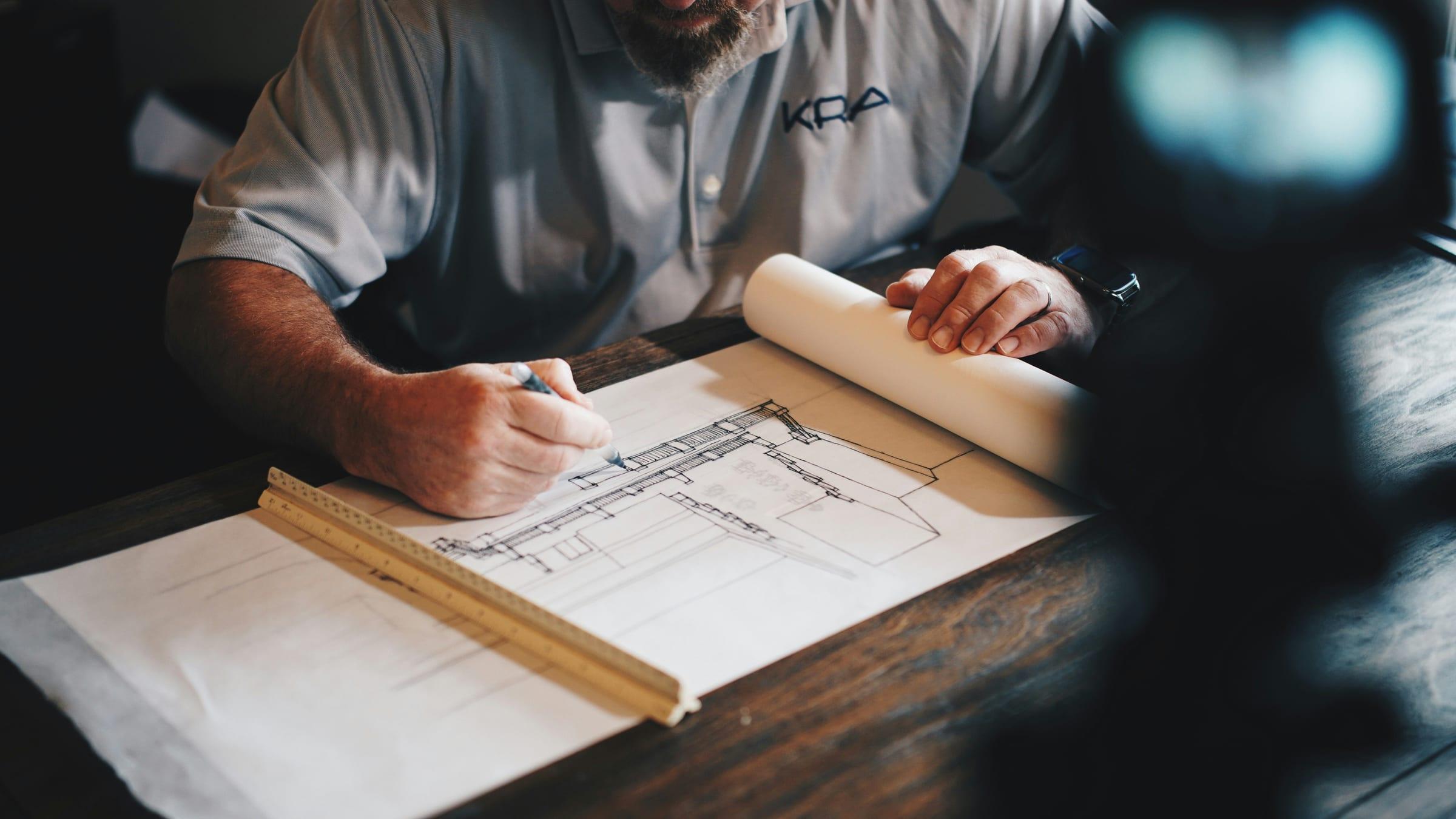 Hands marking up a set of building plans with a ruler.