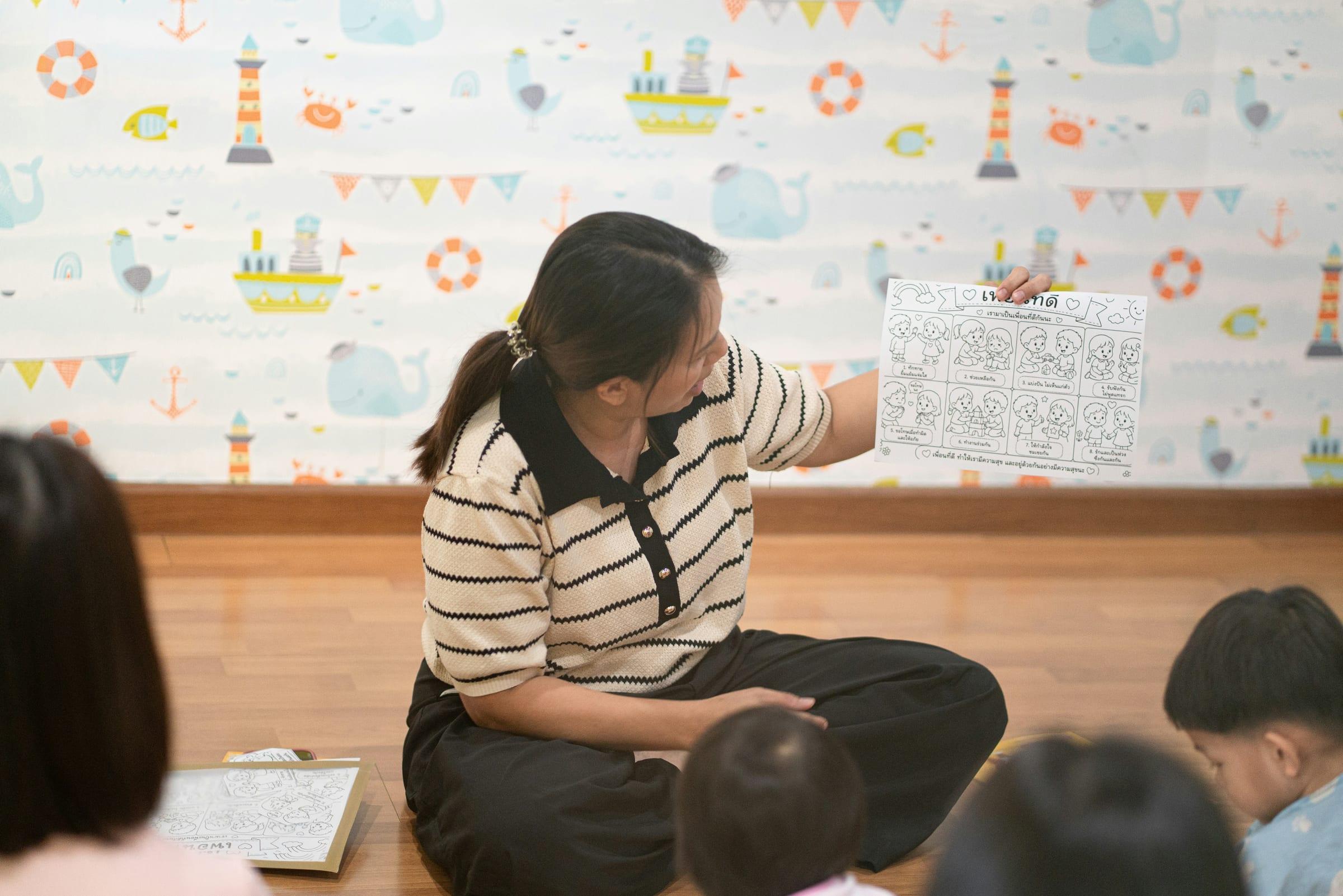 A teacher holding up a picture book to a group of seated children.
