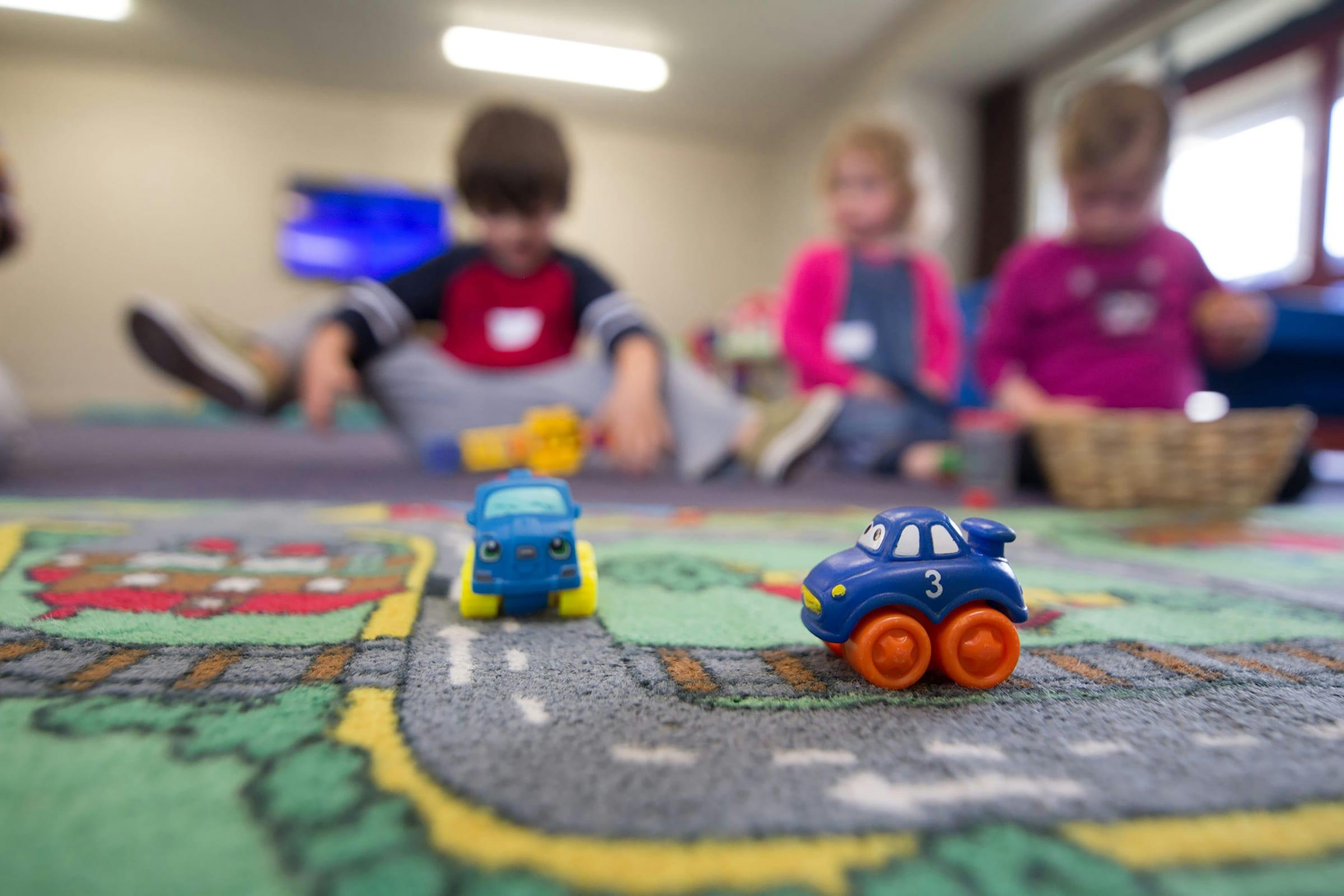 Toddlers playing with toy cars on a patterned mat.