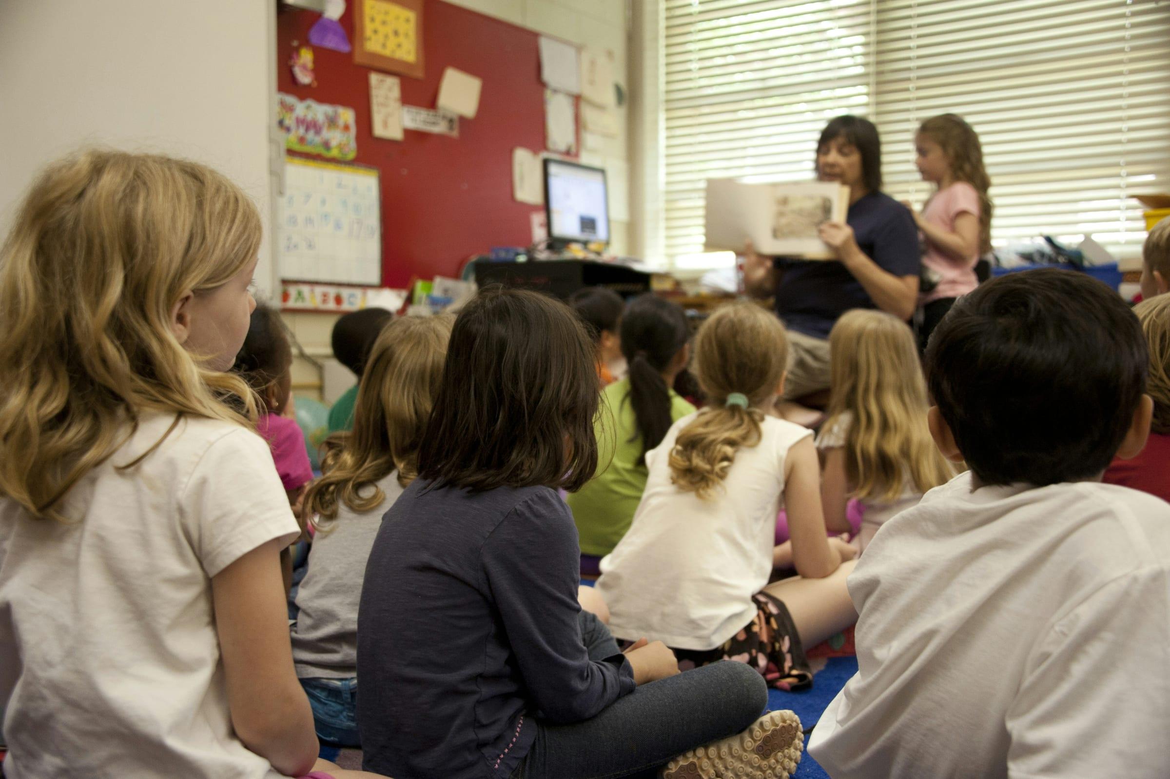A teacher reading to a group of children seated on a classroom floor.