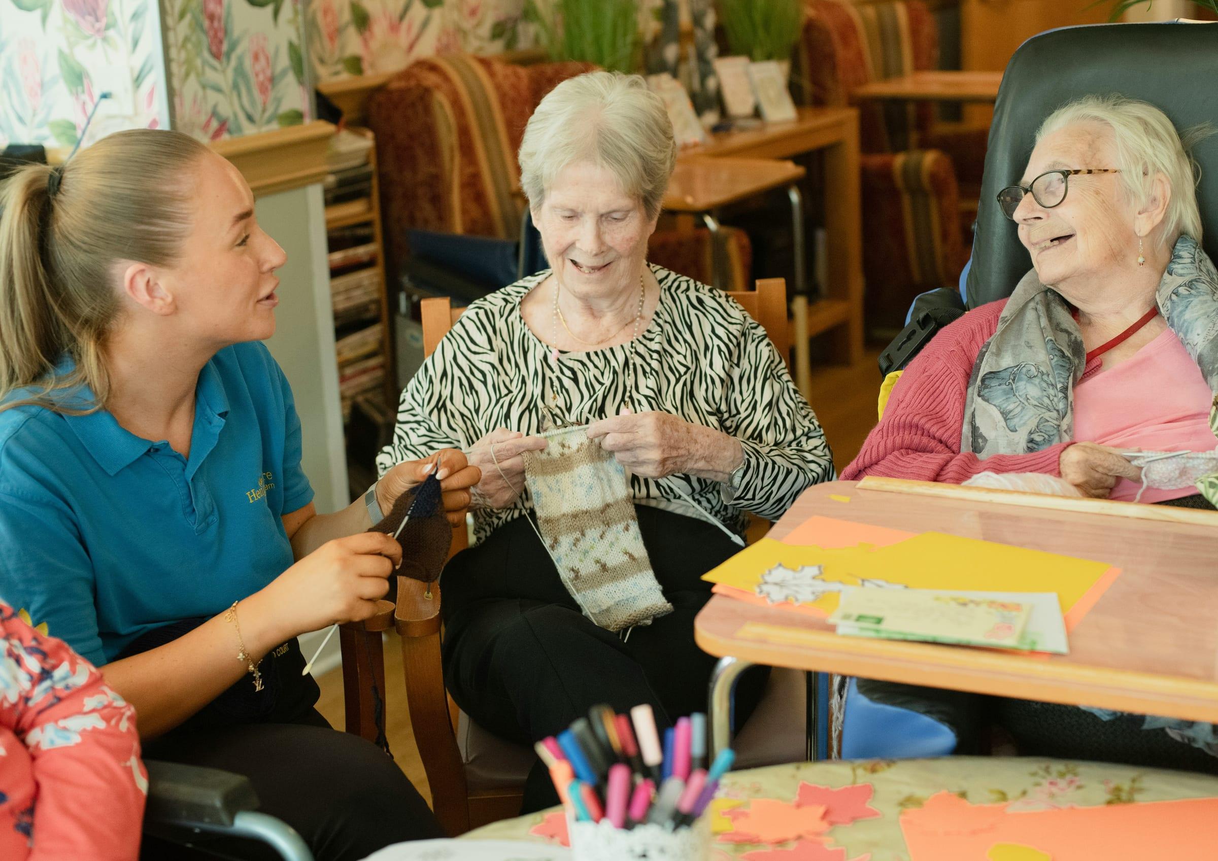 A care worker sitting with residents during a craft activity.