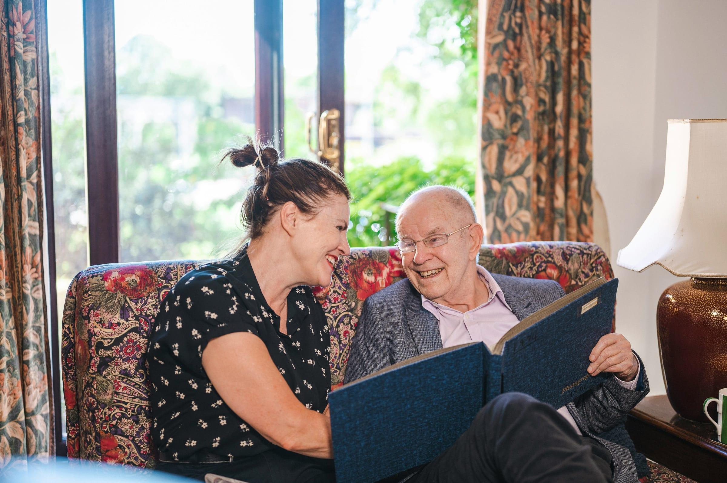 A support worker and an older man laughing together over a photo album.