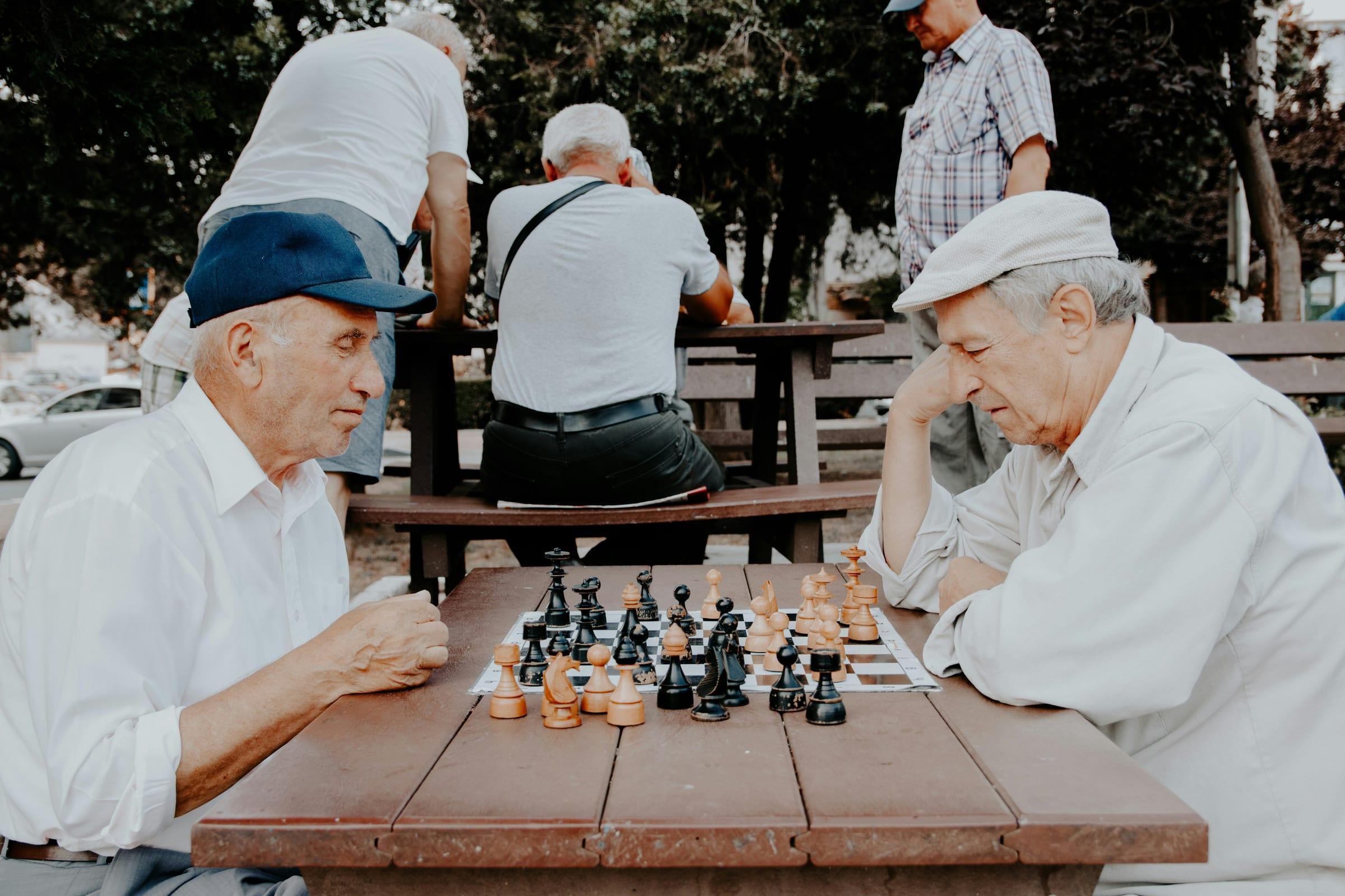 Two older men playing chess at an outdoor table.