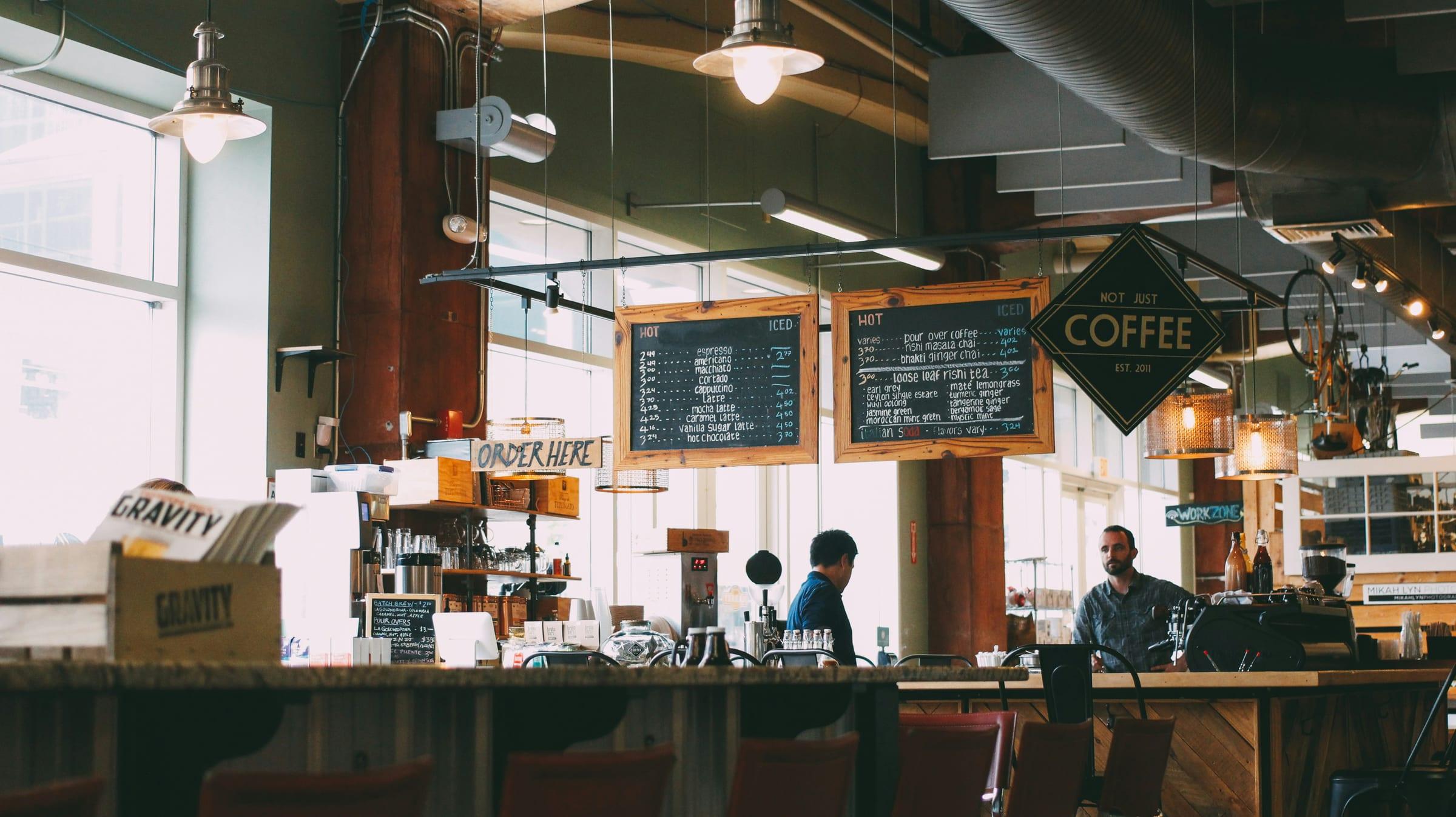 Staff working behind the counter of a cafe, with menu boards above.